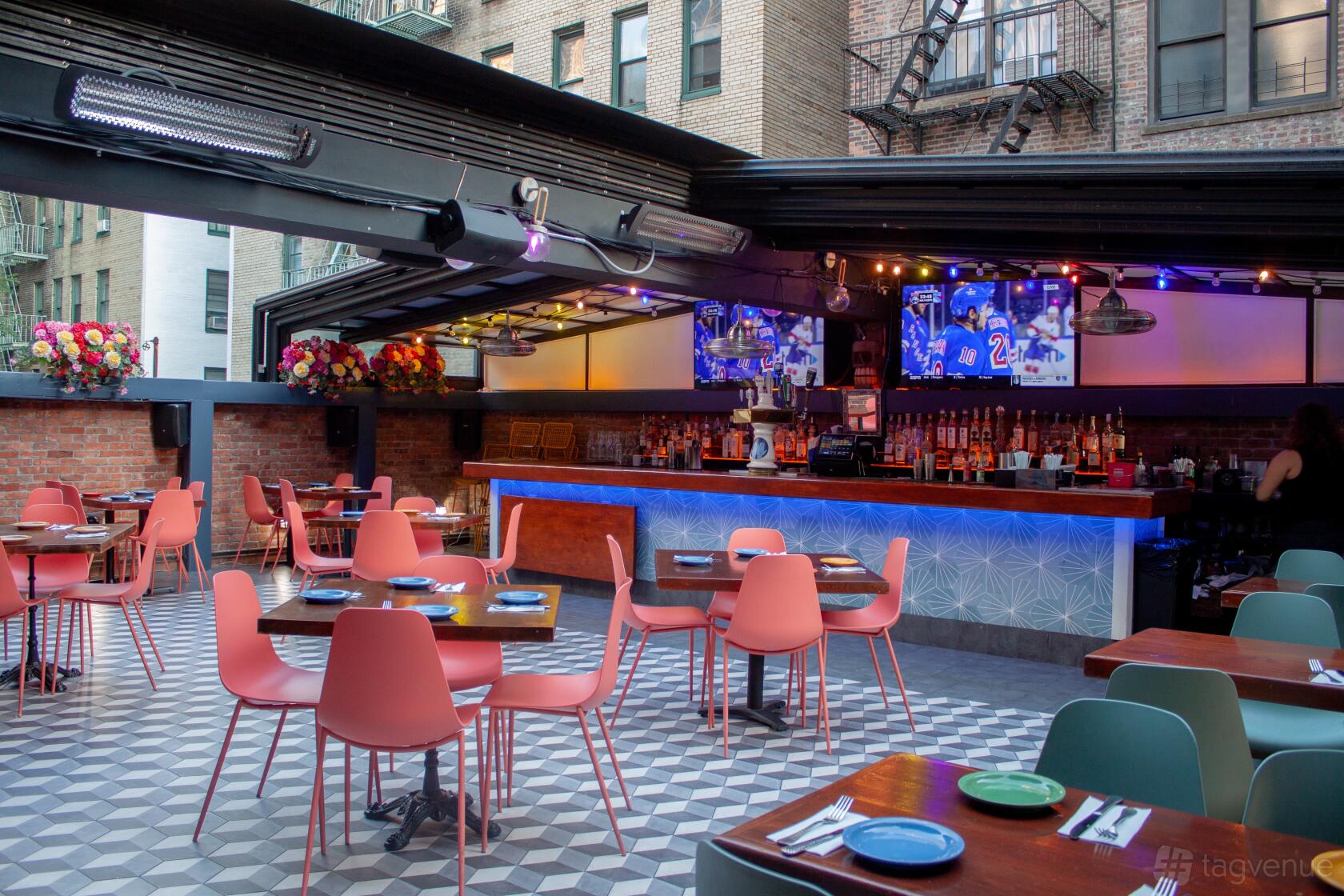 A rooftop restaurant patio with retractable roof, illuminated bar, patterned floor tiles, and pink chairs at Backstage Tavern.