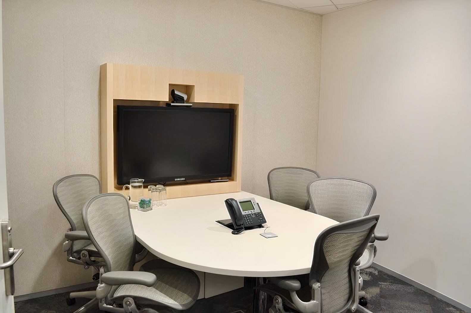 A meeting room with a wall-mounted screen, a conference phone, and mesh chairs at 1 Bligh Street.