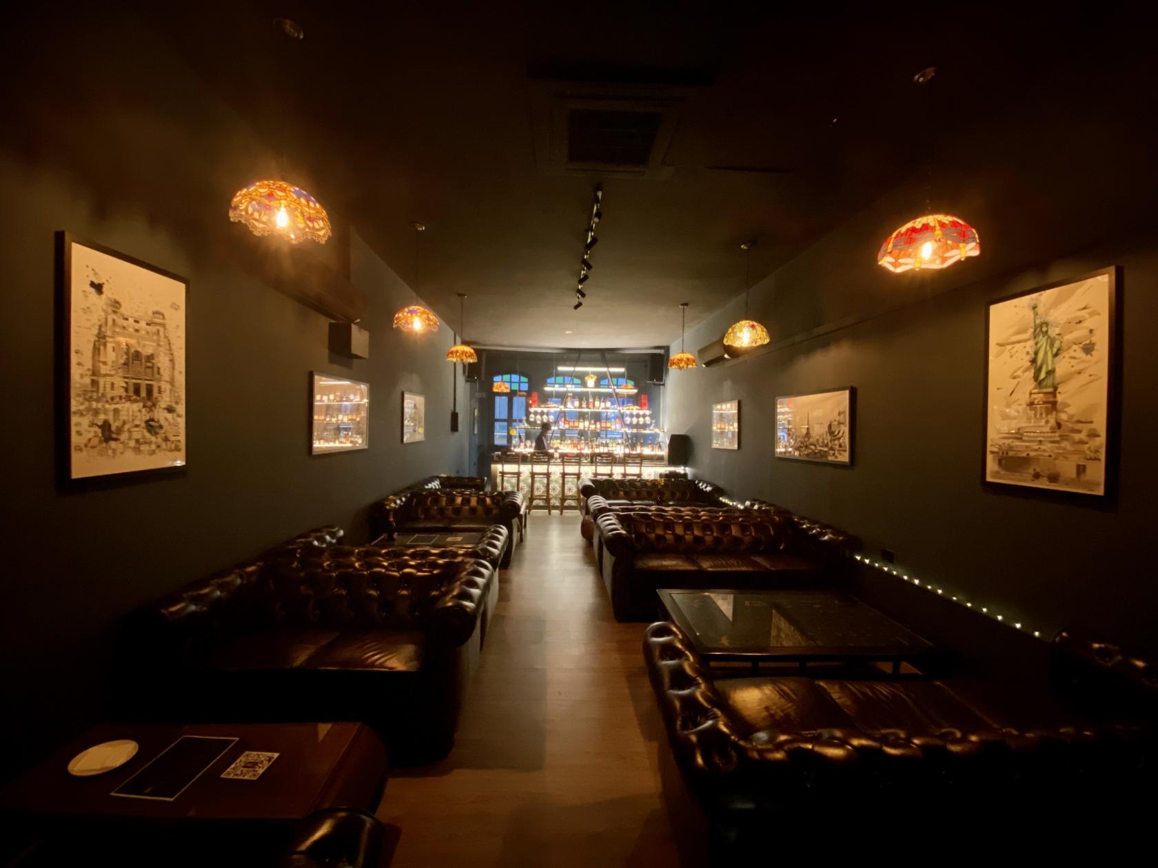 A bar with leather sofas, dim pendant lighting, and framed wall art at The Hidden Story Speakeasy Katong.