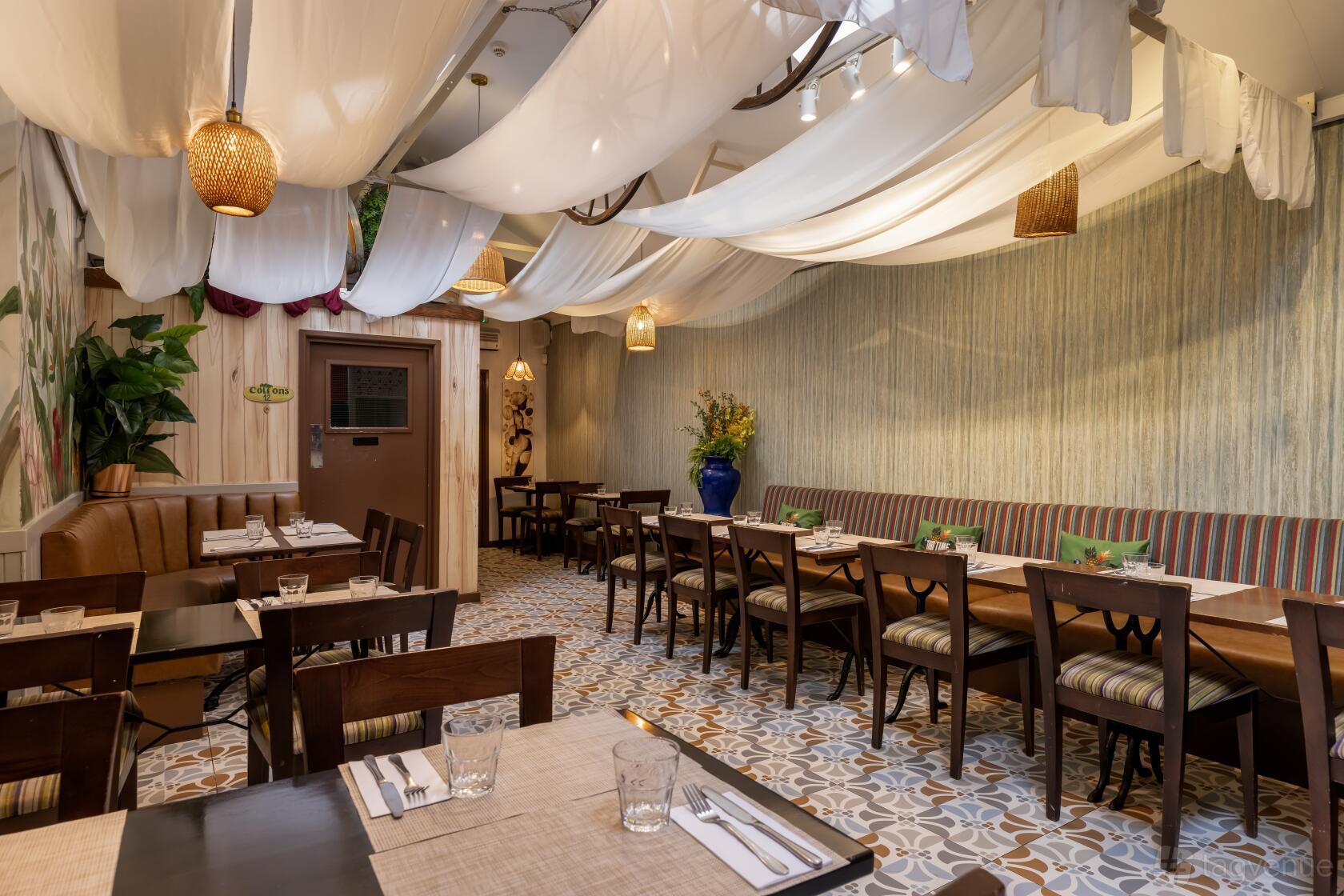 A dining room with draped white fabric ceiling, patterned tile floor, and wooden tables at Cottons Camden.
