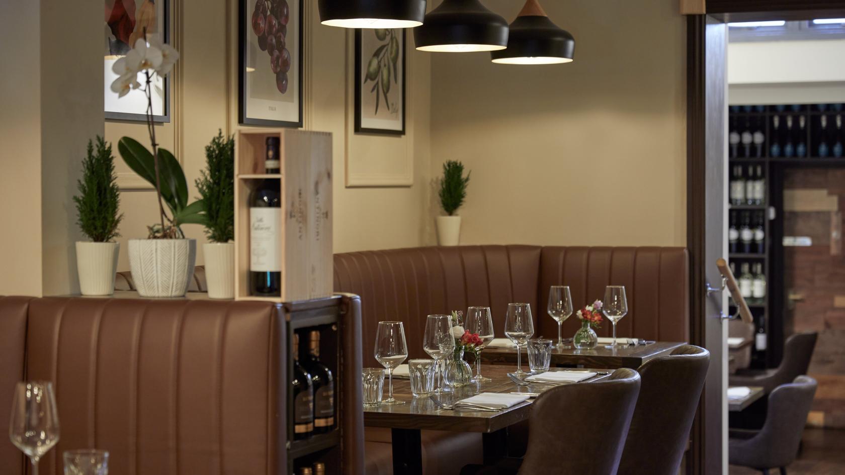 A restaurant with brown leather booths, framed artwork, pendant lights, and set tables at Bacco Ristorante Italiano.