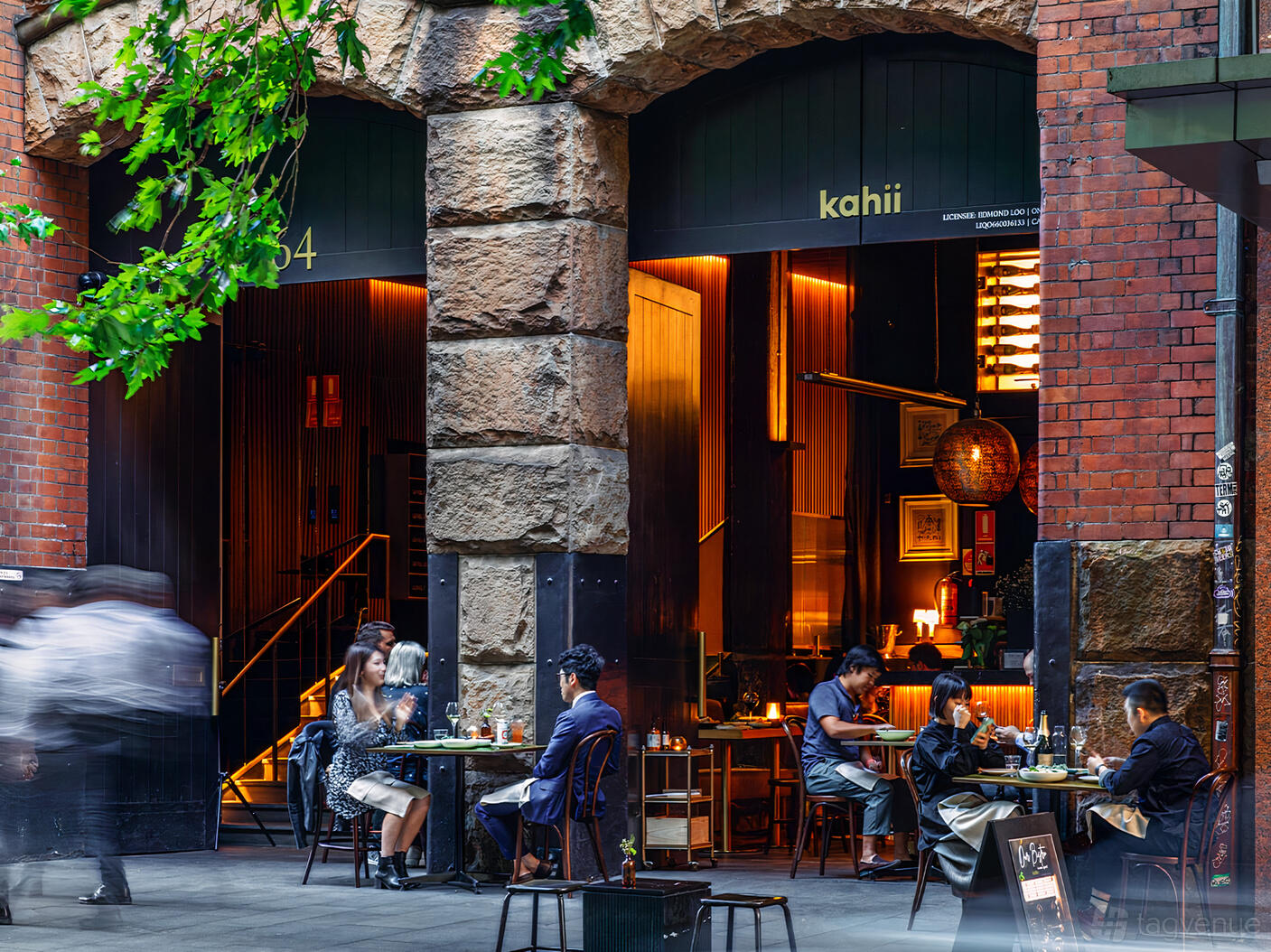A cozy bar with exposed brick arches, warm lighting, and small outdoor tables at KAHII | Kissaten & Wine Bar.