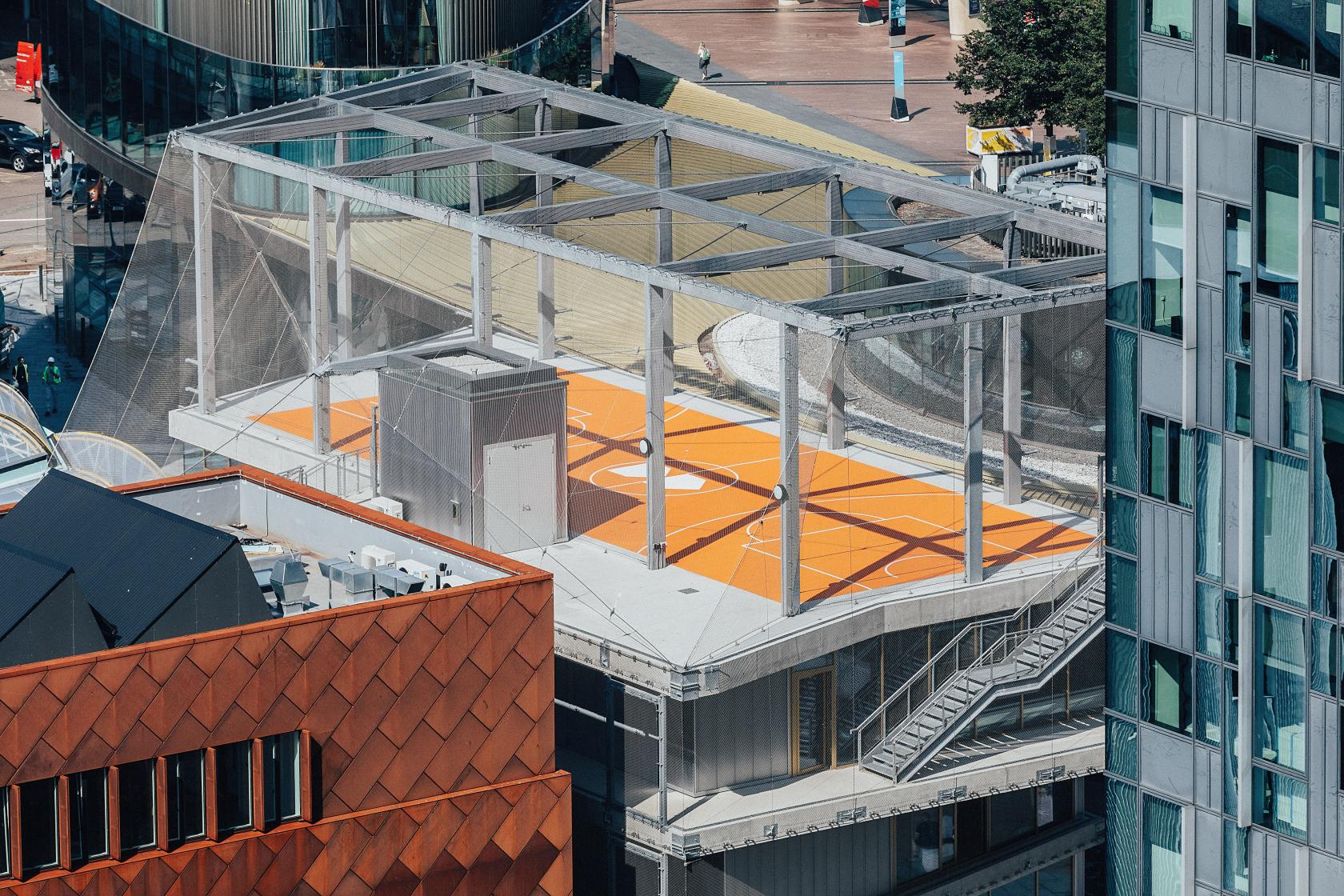 A rooftop basketball court with orange flooring, a metal frame canopy, and city views at Design District.