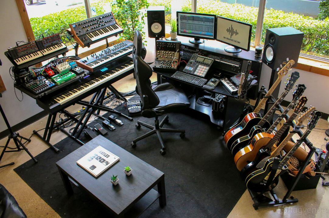 A music studio with multiple synthesizers, mixing consoles, and guitars near large windows at The Creatives Factory.