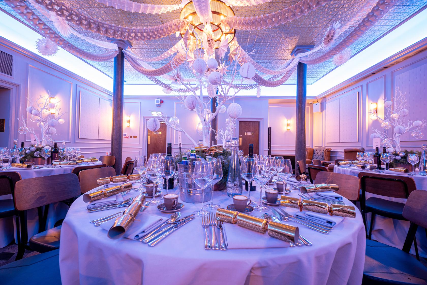 A function room with round tables set for dining, decorative ceiling drapes, and ambient lighting at The Brewery.