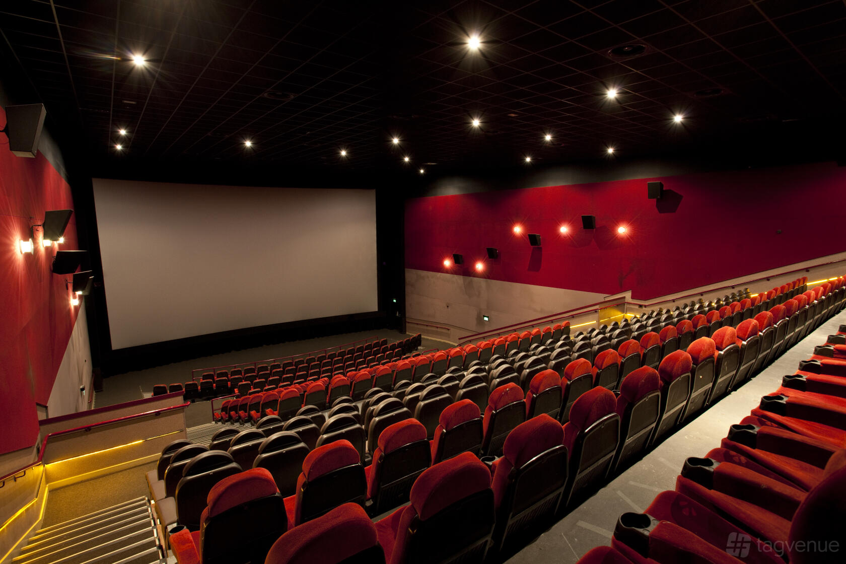 A cinema with tiered red and black seating, wall sconces, and a large projection screen at ODEON LUXE Birmingham Broadway Plaza.