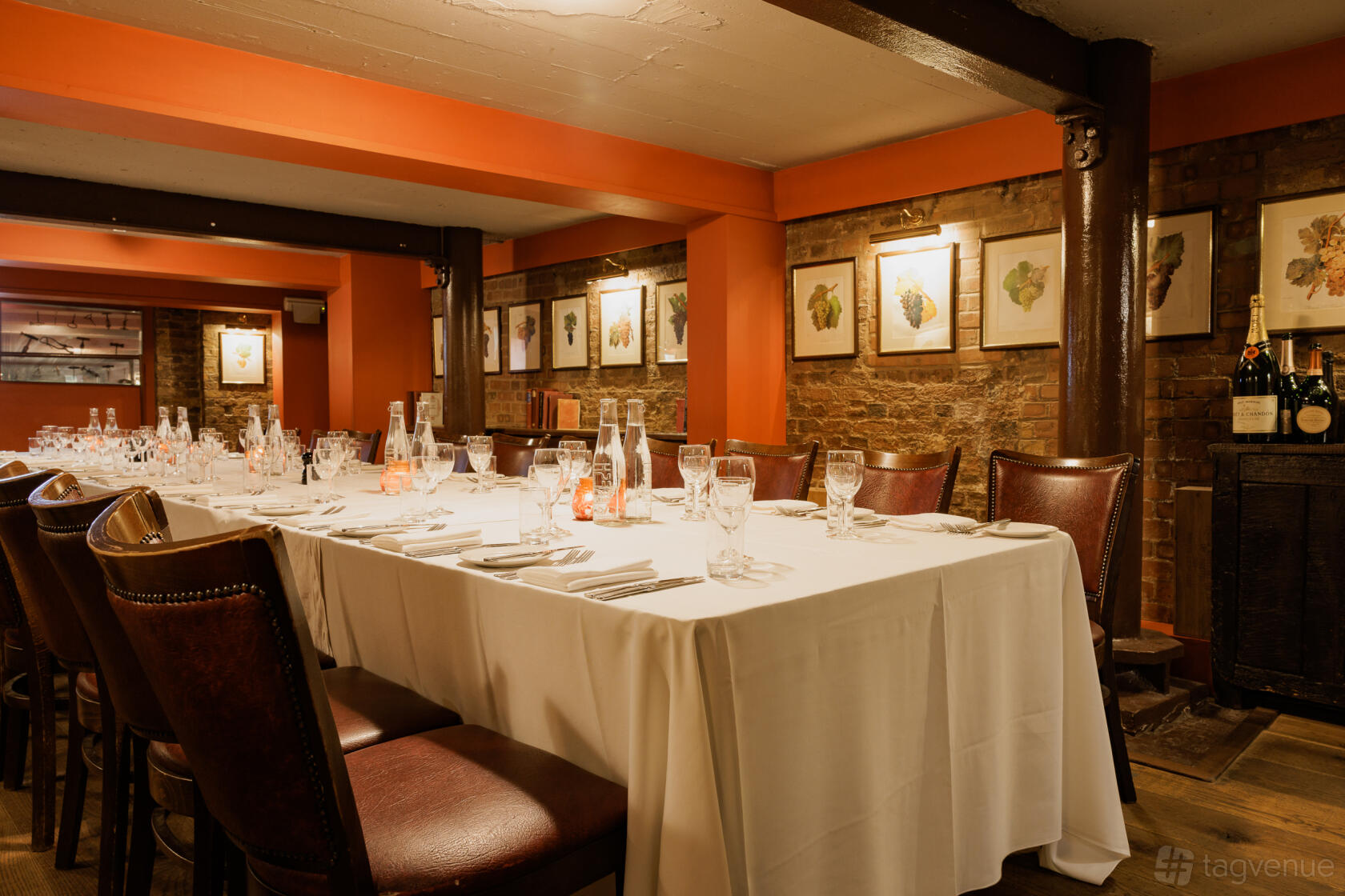 A restaurant cellar with brick walls, framed botanical prints, and a long table set with glassware at Bleeding Heart.