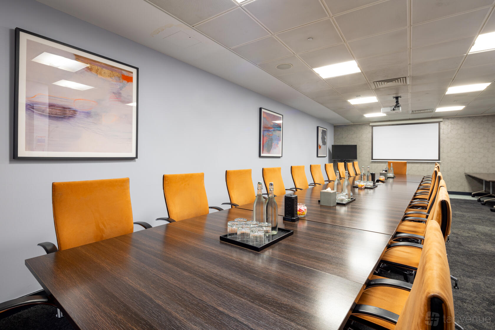 A meeting room with a long dark wood table, orange chairs, wall art, and a projector screen at Landmark: Royal Exchange, Bank, London.