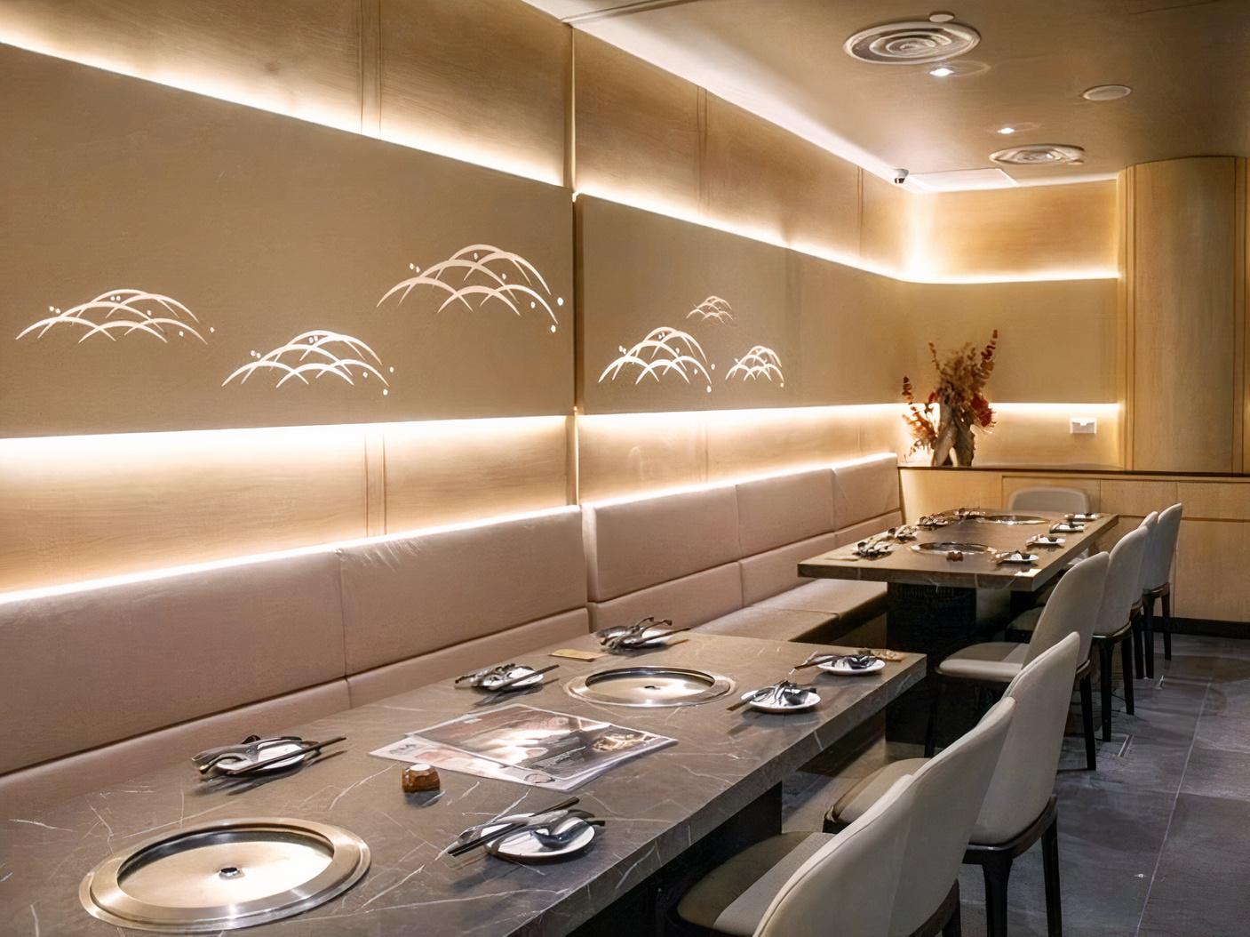 A restaurant dining room with built-in hot pot tables, upholstered bench seating, and wall-mounted accent lighting at TAJIMAYA - VIVO CITY BRANCH.