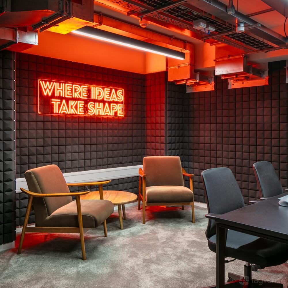 A podcast studio with acoustic foam panels, mid-century armchairs, and a neon sign reading 'Where Ideas Take Shape' at Spacemade - Beton.