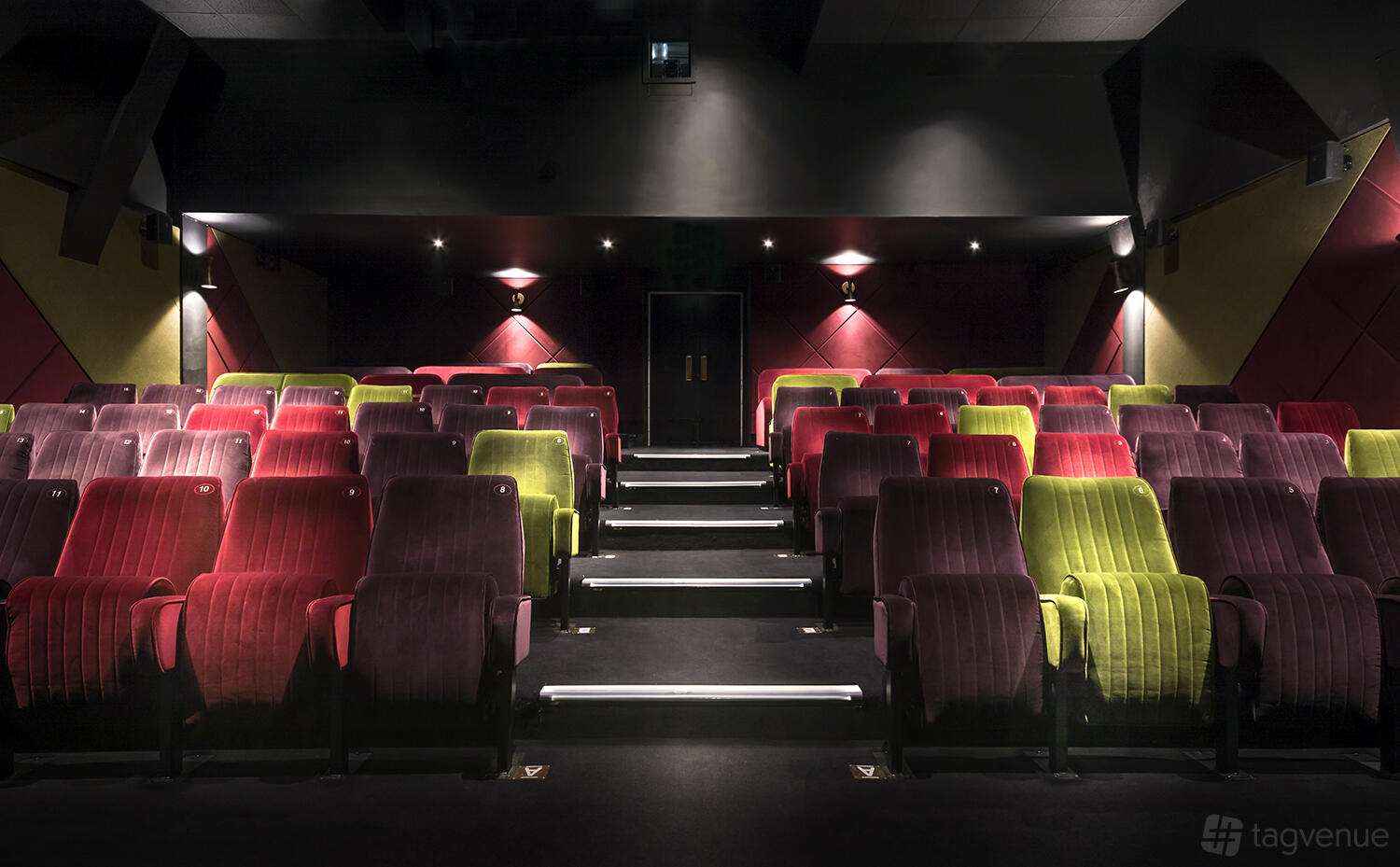 An auditorium with tiered rows of plush red and green velvet seats and soft wall lighting at Everyman Reigate.