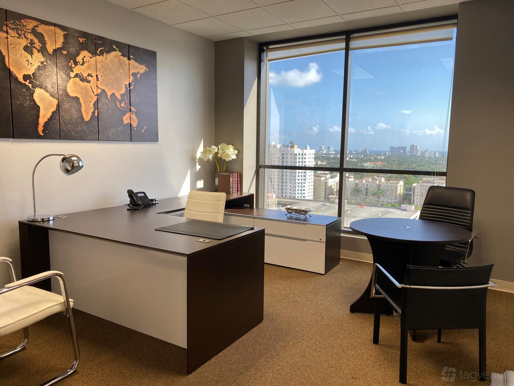 An office space with a large desk, round meeting table, and floor-to-ceiling windows at Empire Executive Offices, Fort Lauderdale.