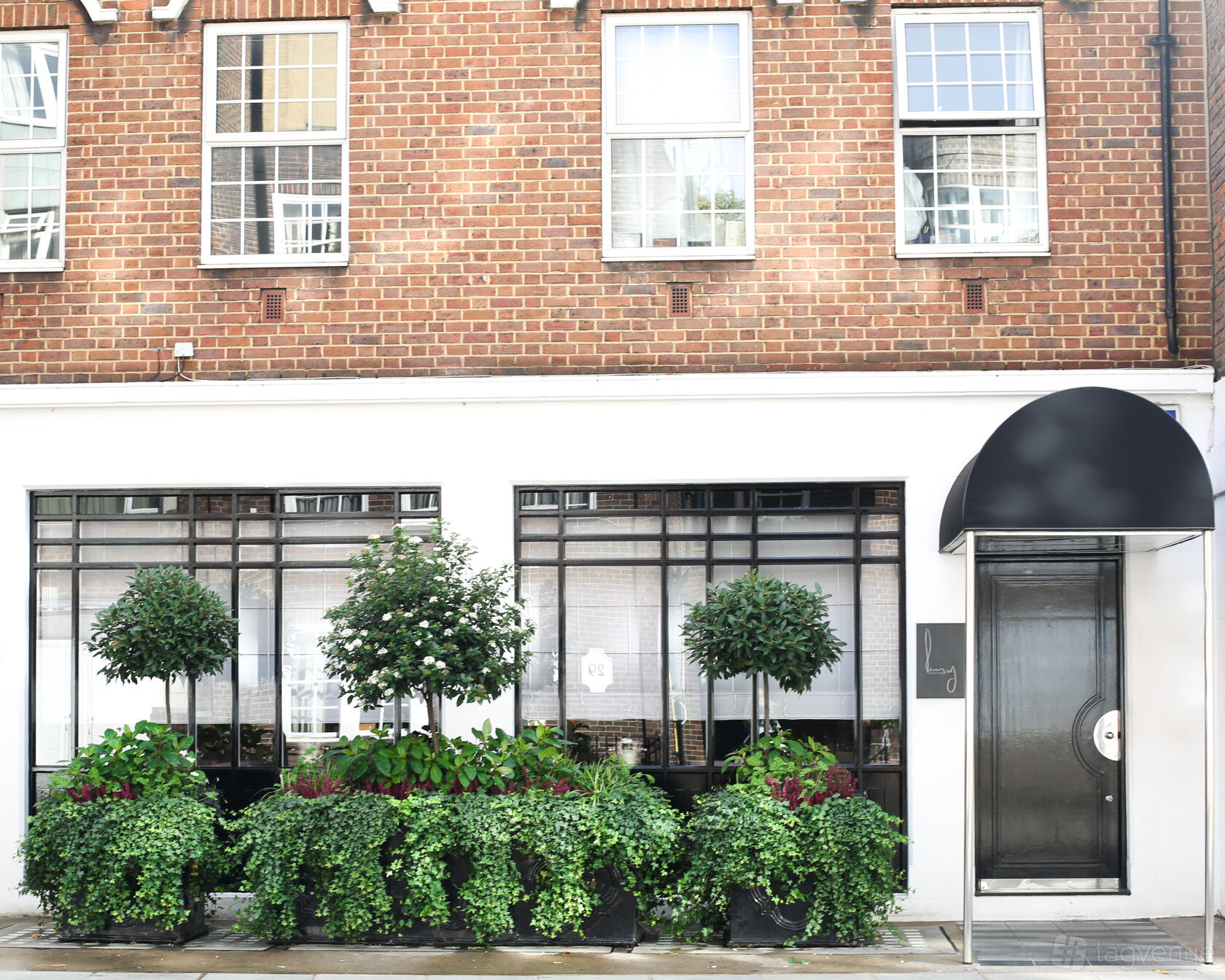 A restaurant with large black-trimmed windows, brick facade, and potted green plants at Restaurant Gordon Ramsay.