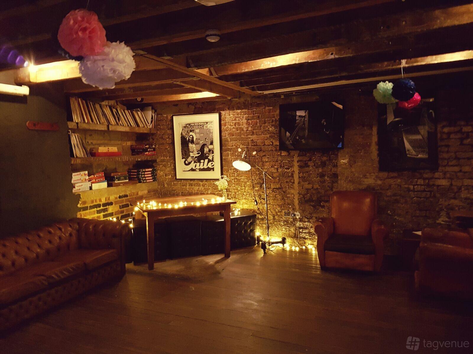 A basement bar with exposed brick walls, leather armchairs, board games, and string lights at The Gallery.