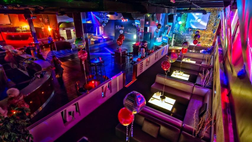 A nightclub lounge with plush booths, glowing tables, disco balls, and colorful LED lighting at District Lounge.