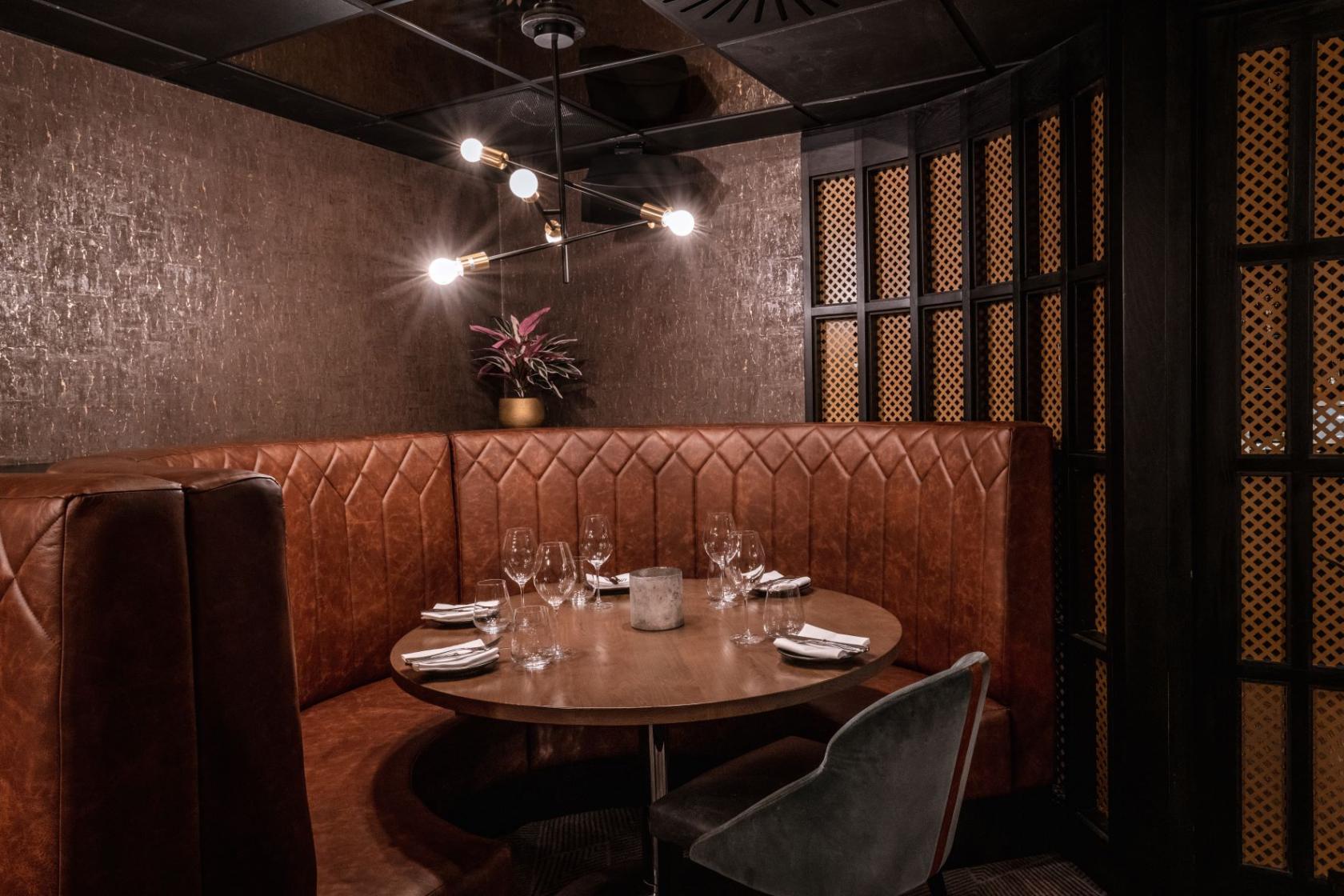 A restaurant with a round table, leather upholstered booth seating, and modern pendant lighting at Gaucho Leeds.