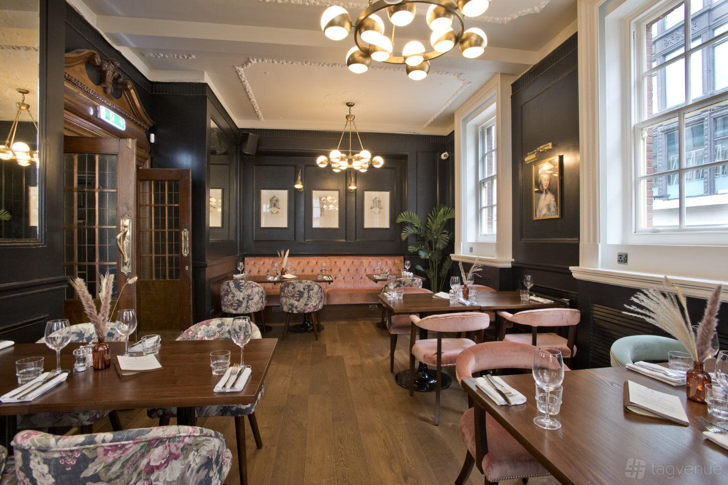 A pub dining room with blush velvet chairs, wooden tables, and large windows at The Duchess.