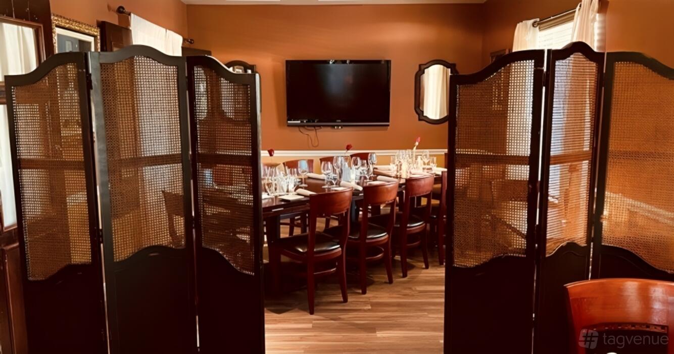 A dining room with a long table set for guests, wood chairs, folding privacy screens, and wall-mounted TV at Vienna Wine Bar.