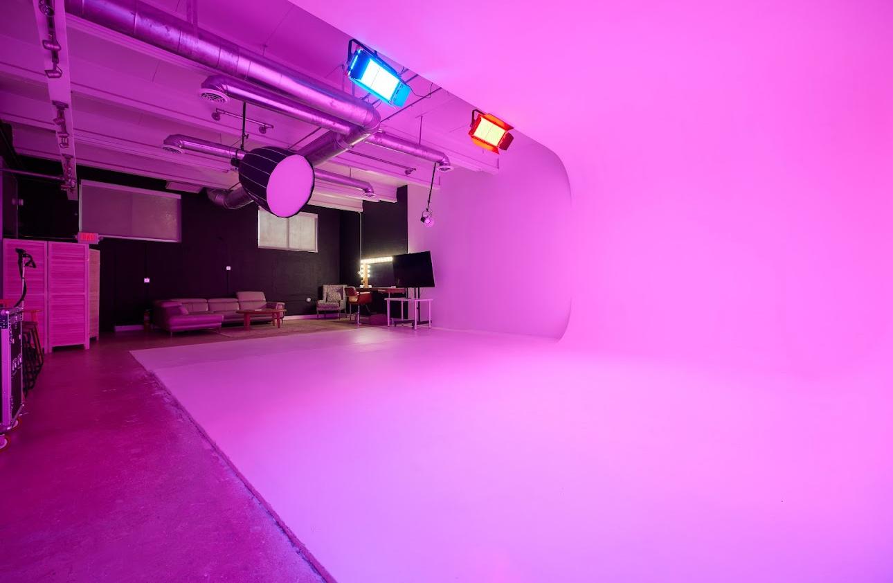 A photo studio with a large white cyclorama wall, colored lighting, and lounge seating at Bey Studios.