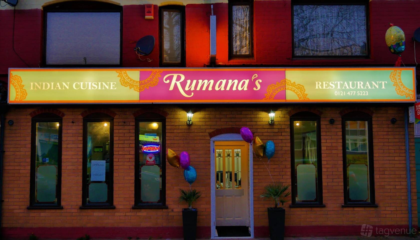 A restaurant exterior with a colorful sign, brick facade, potted plants, and balloons at Rumana's.