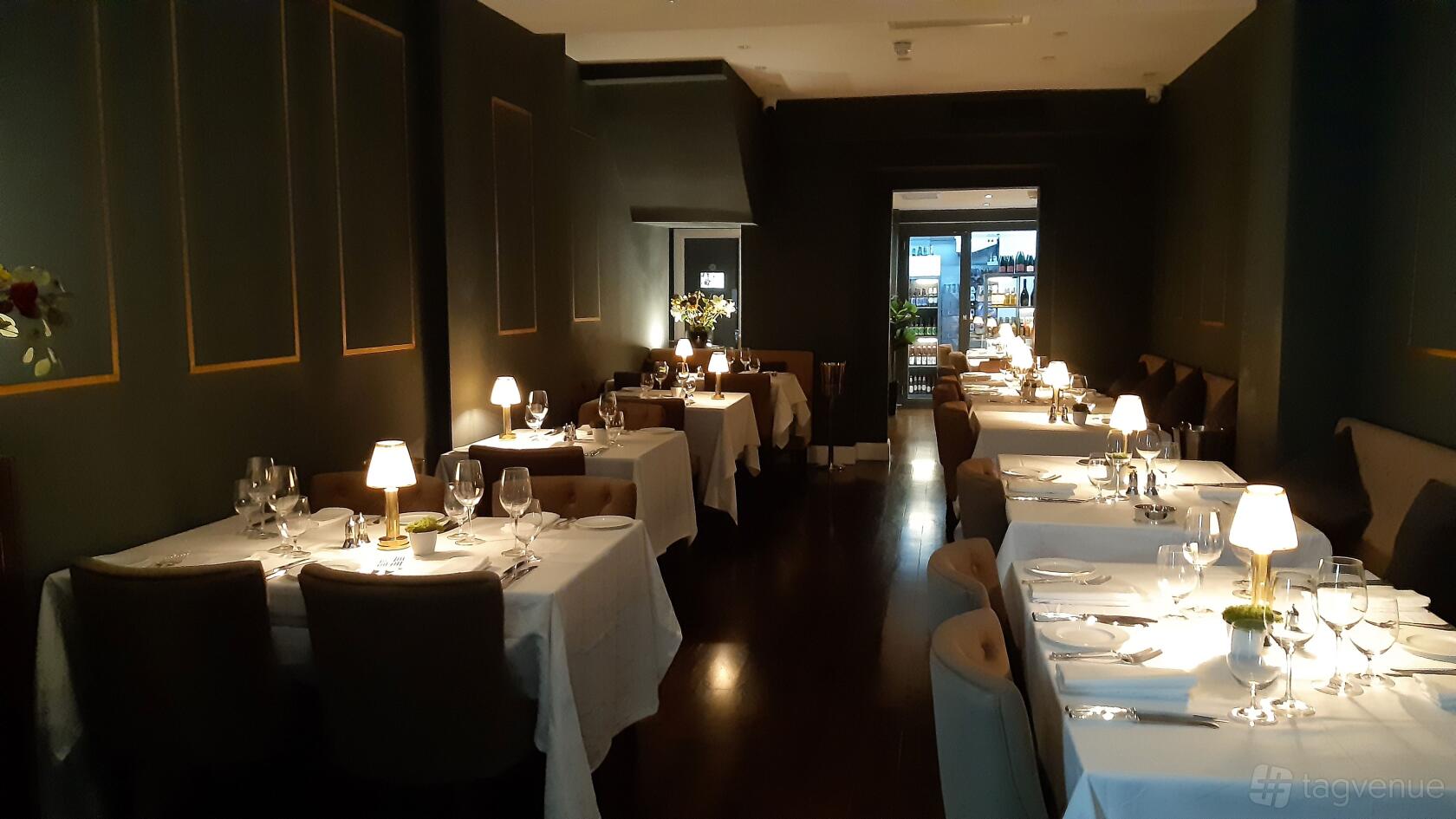 A restaurant dining area with white tablecloths, cushioned chairs, and soft lamp lighting at Jamuna.