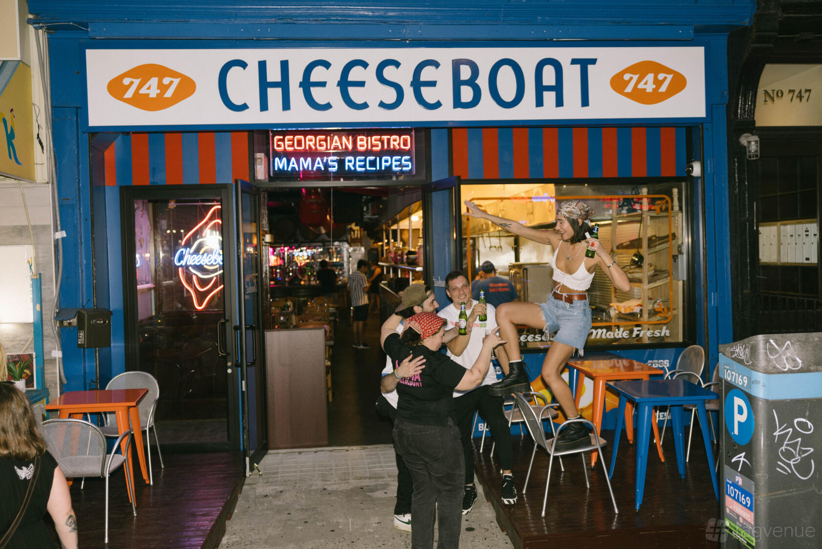 A restaurant with blue exterior, striped awning, and outdoor tables at Cheeseboat Manhattan.