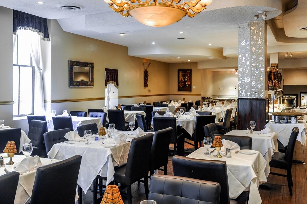 A restaurant dining area with white tablecloths, dark leather chairs, and decorative lighting at Aroma Fine Indian Cuisine.