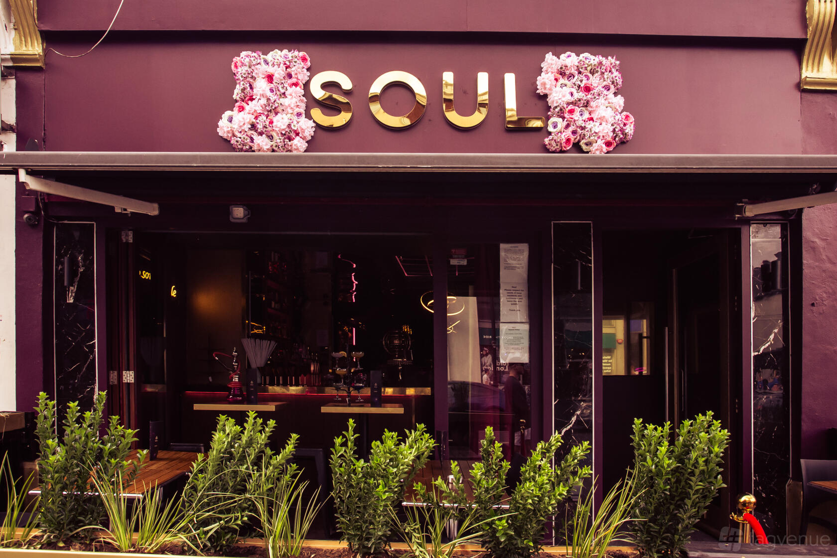 A versatile event space with a deep purple exterior, gold signage, floral decor, and greenery at Soul Lounge.