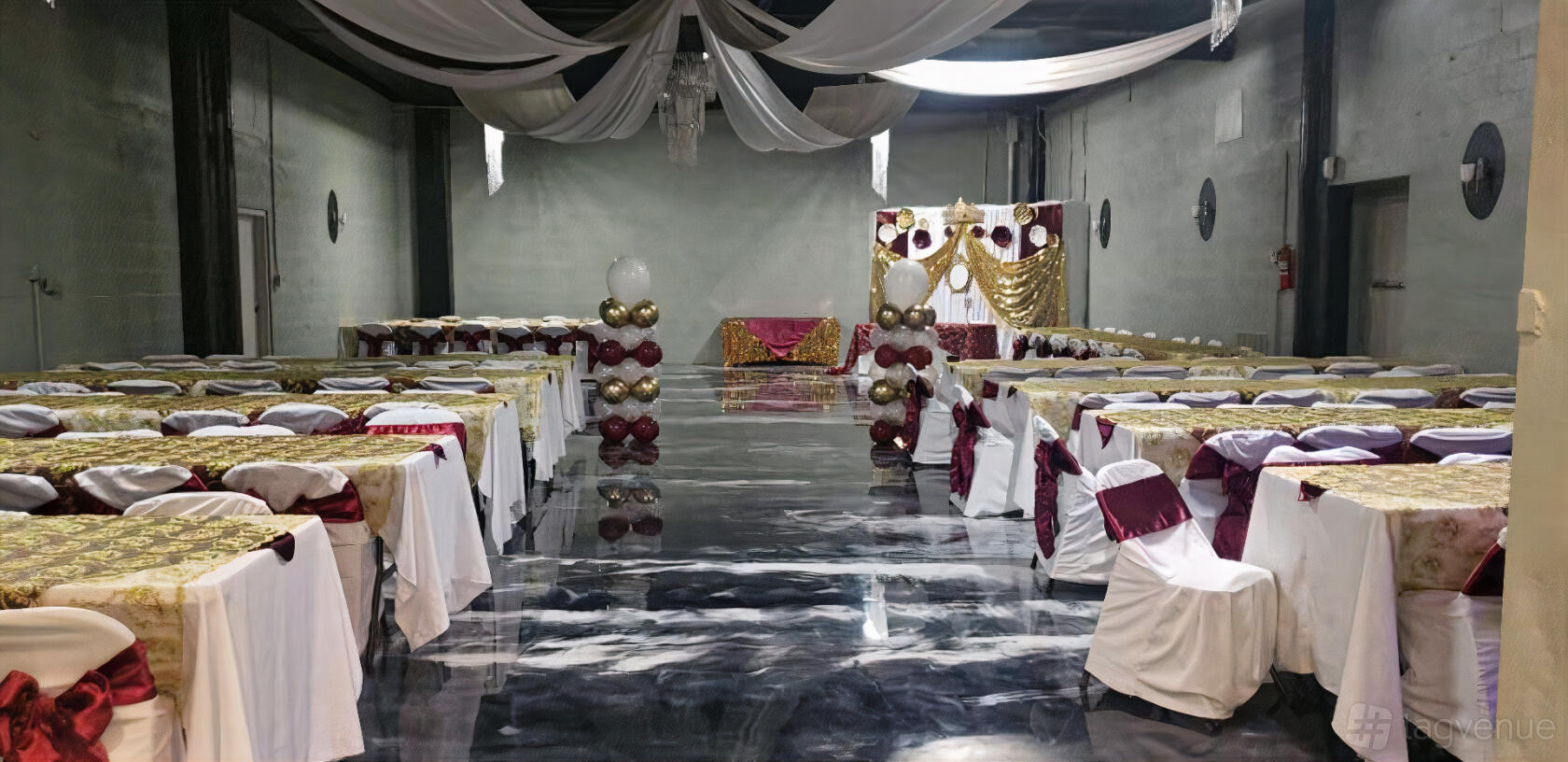 A banquet hall with draped ceilings, polished marble floors, and rows of tables with gold and burgundy decor at Tha Star Place.