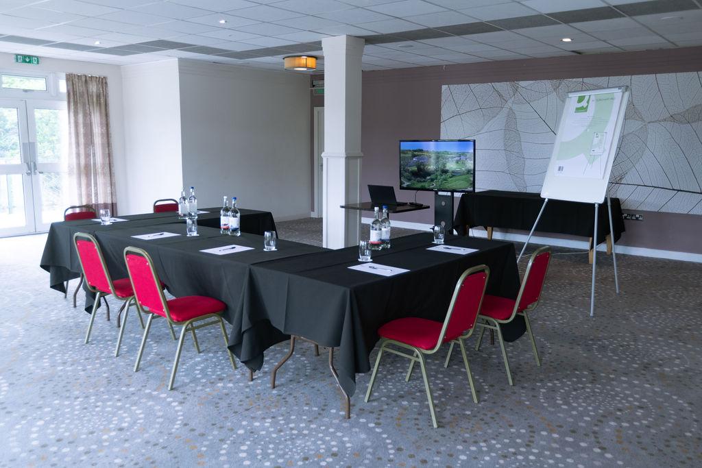 A hotel meeting room with rectangular tables covered in black linens, red chairs, a flip chart, and a TV screen at The Dartmouth Hotel, Golf & Spa.