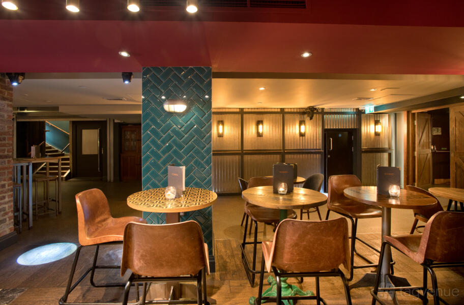 A lounge in a bar with leather chairs, round wooden tables, and teal subway tile accents at Core.