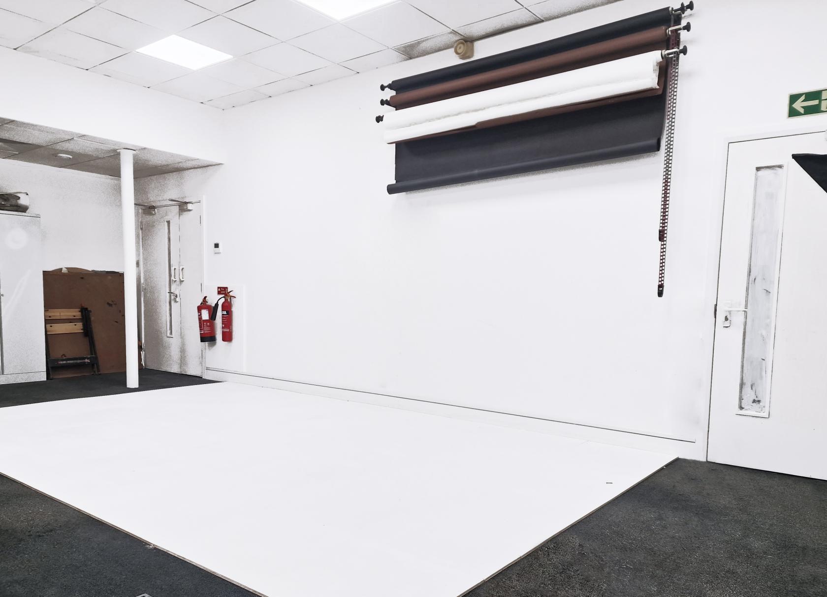 A photo studio with seamless white backdrops, overhead lighting, and wall-mounted paper rolls at Corridor Studio.