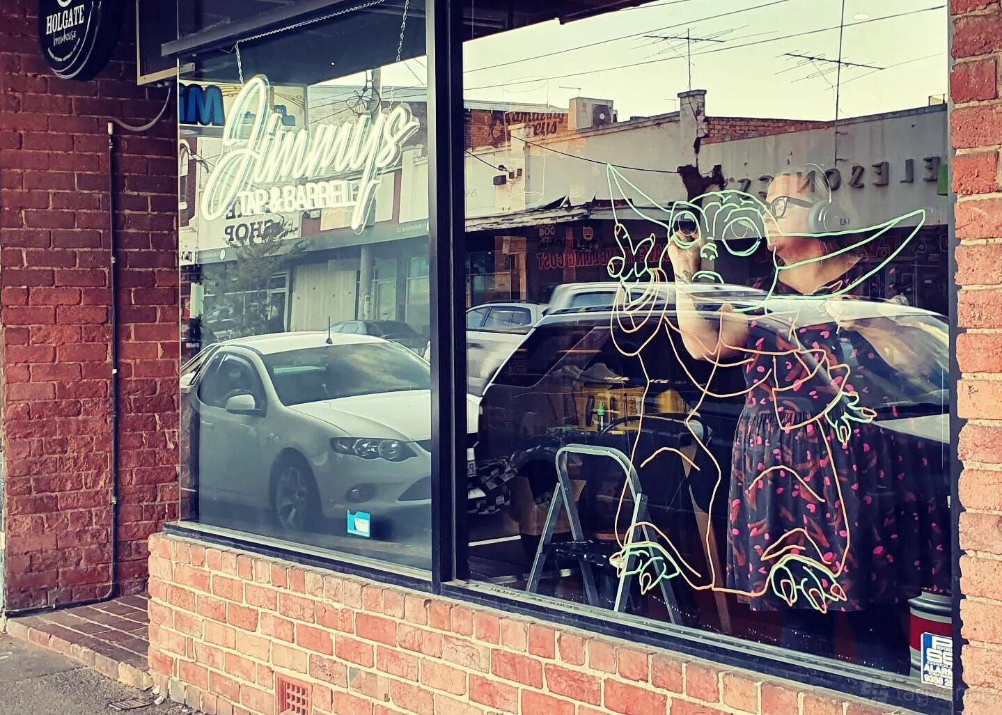 A pub with a brick exterior and large front window featuring a whimsical chalk drawing at Jimmy's Tap & Barrel.
