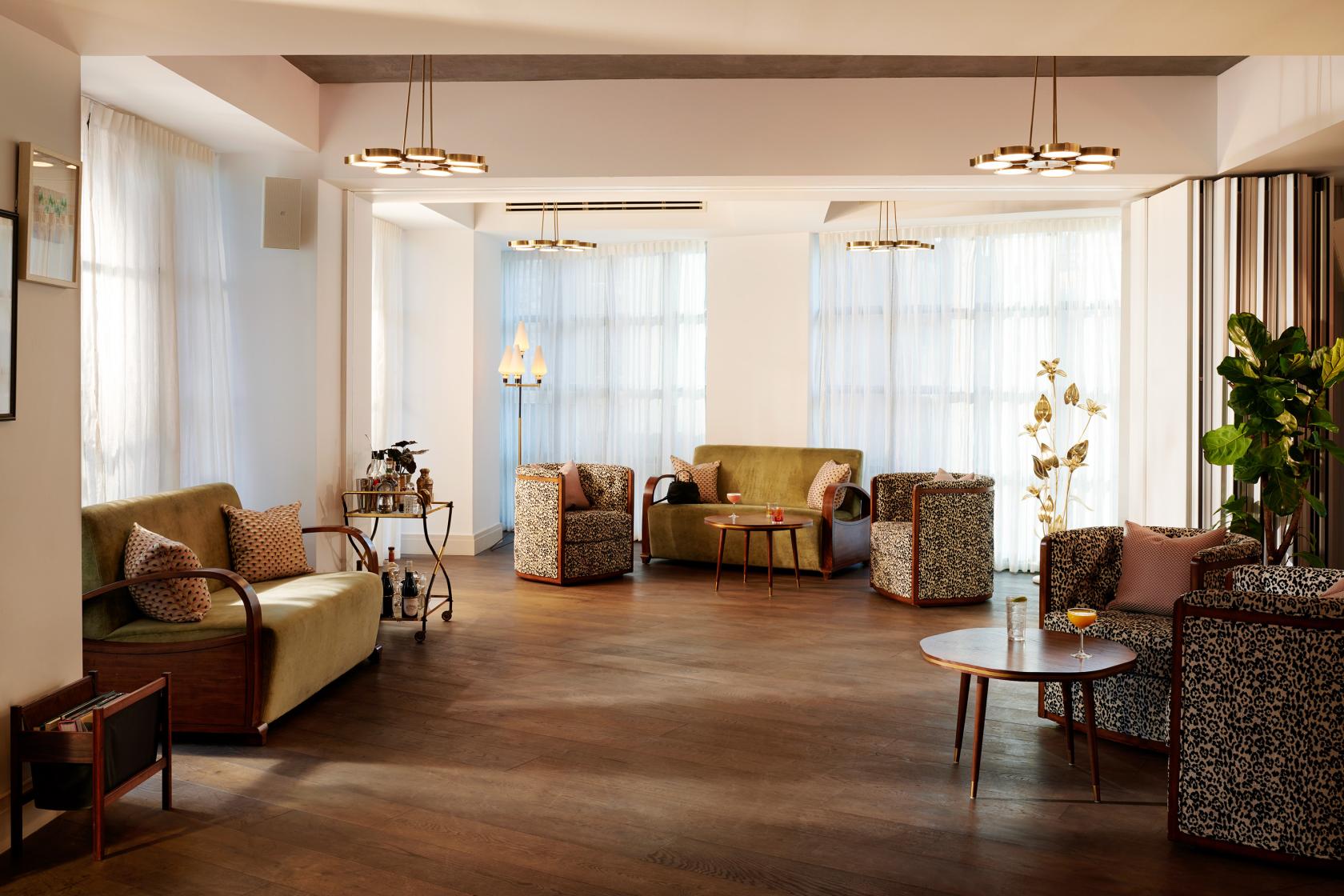An event space in a hotel with floor-to-ceiling windows, wooden floors, cushioned seating, and modern lighting at The Hoxton, Southwark.