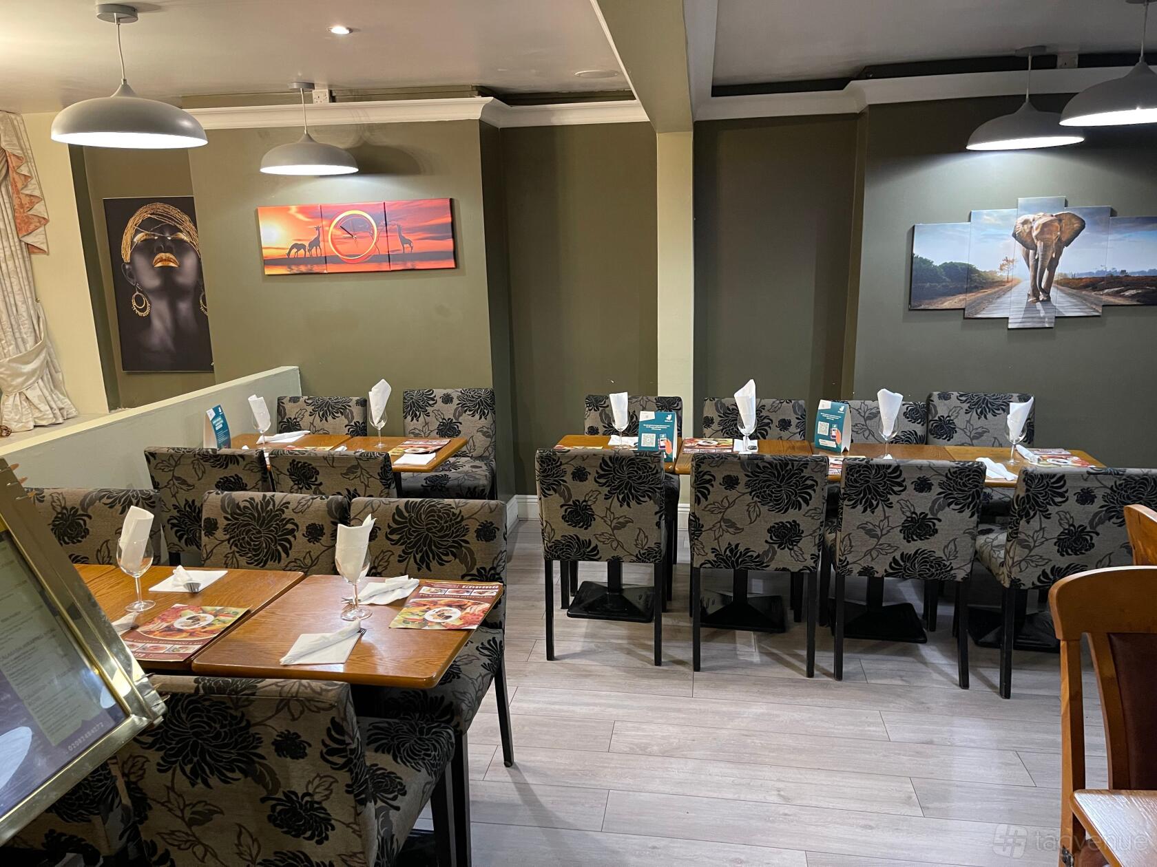 A restaurant dining area with patterned upholstered chairs, wooden tables, and African-themed artwork at Calabash Restaurant & Bar.