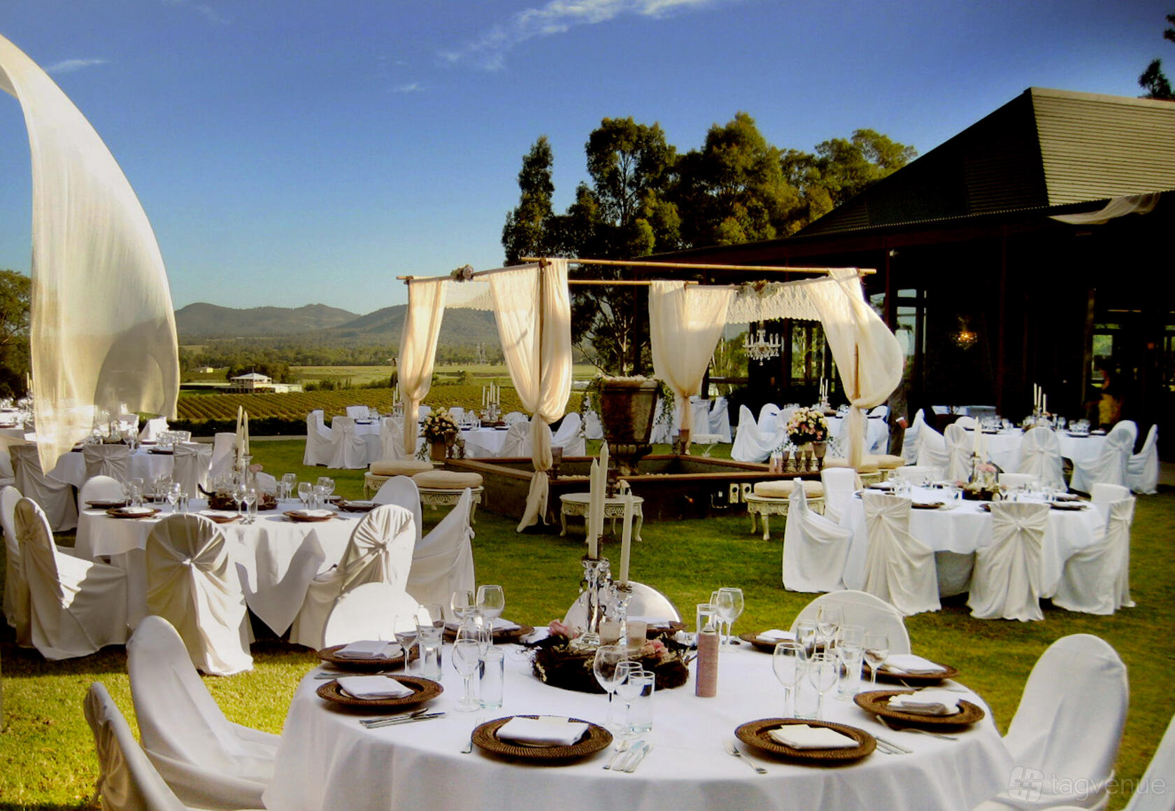 An outdoor courtyard with round tables covered in white linens, draped canopy, and vineyard views at Estate Tuscany Hunter Valley.