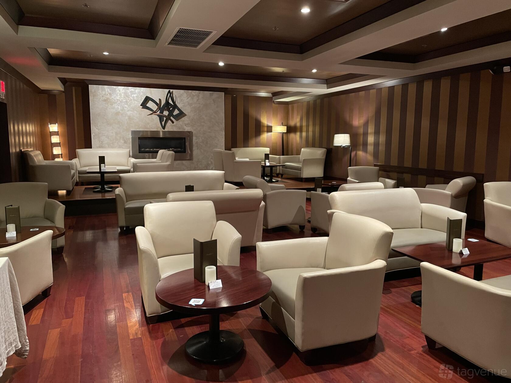A restaurant lounge with cream leather armchairs, round wooden tables, and striped brown walls at Amelia's.