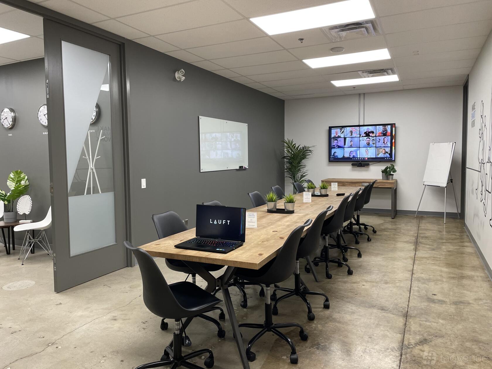 A coworking space with a long wooden table, office chairs, wall-mounted screen, and whiteboards at LAUFT Burlington Centre.
