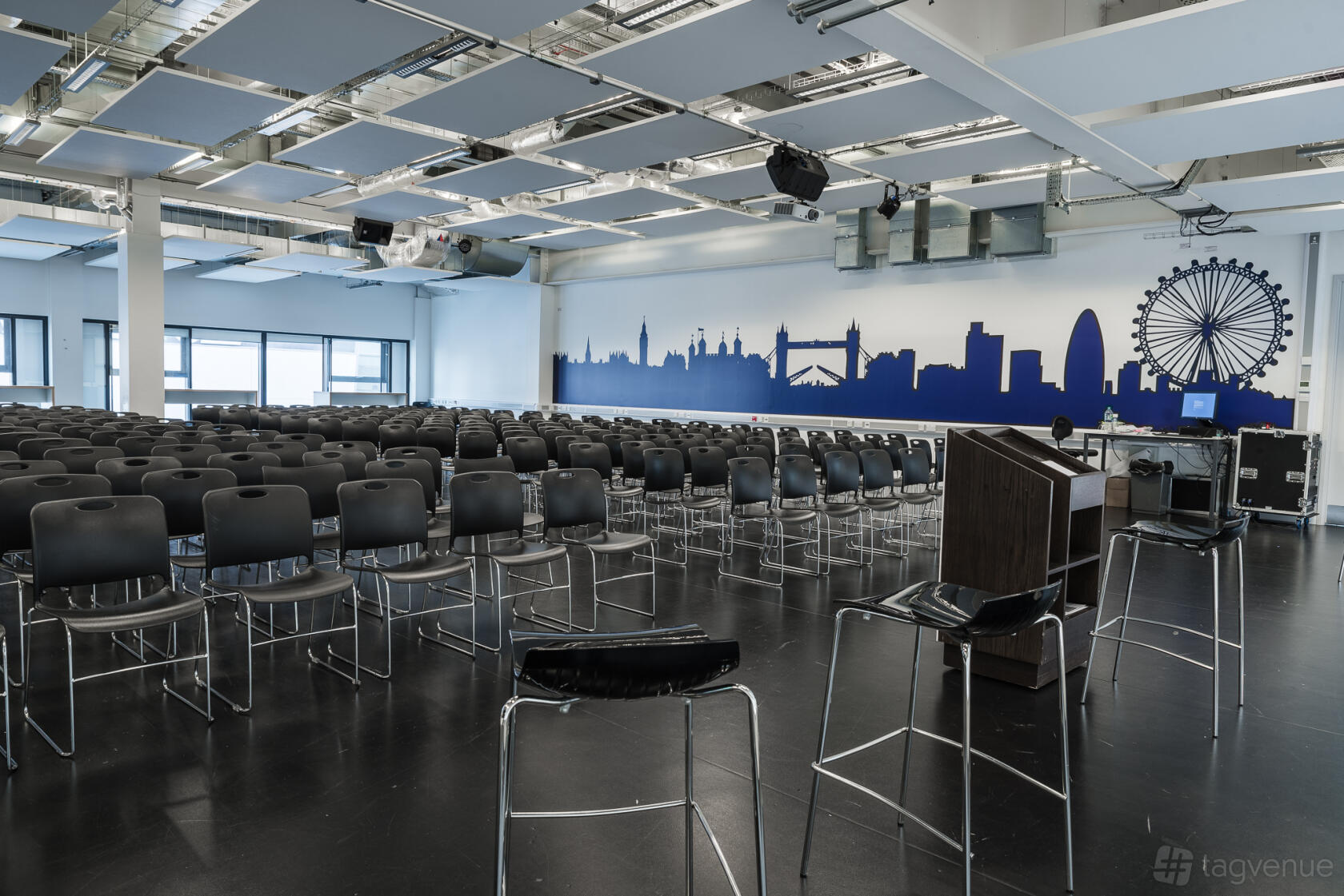 A spacious school hall with rows of black chairs, a lectern, and a London skyline mural at London Academy of Excellence Tottenham.