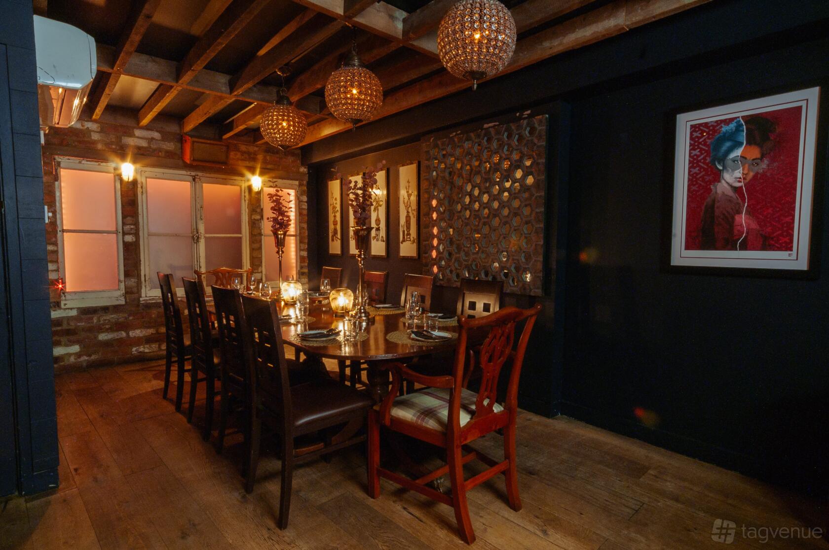 A private dining room with a large wooden table, candlelit place settings, exposed brick walls, and decorative pendant lights at The Last Talisman.