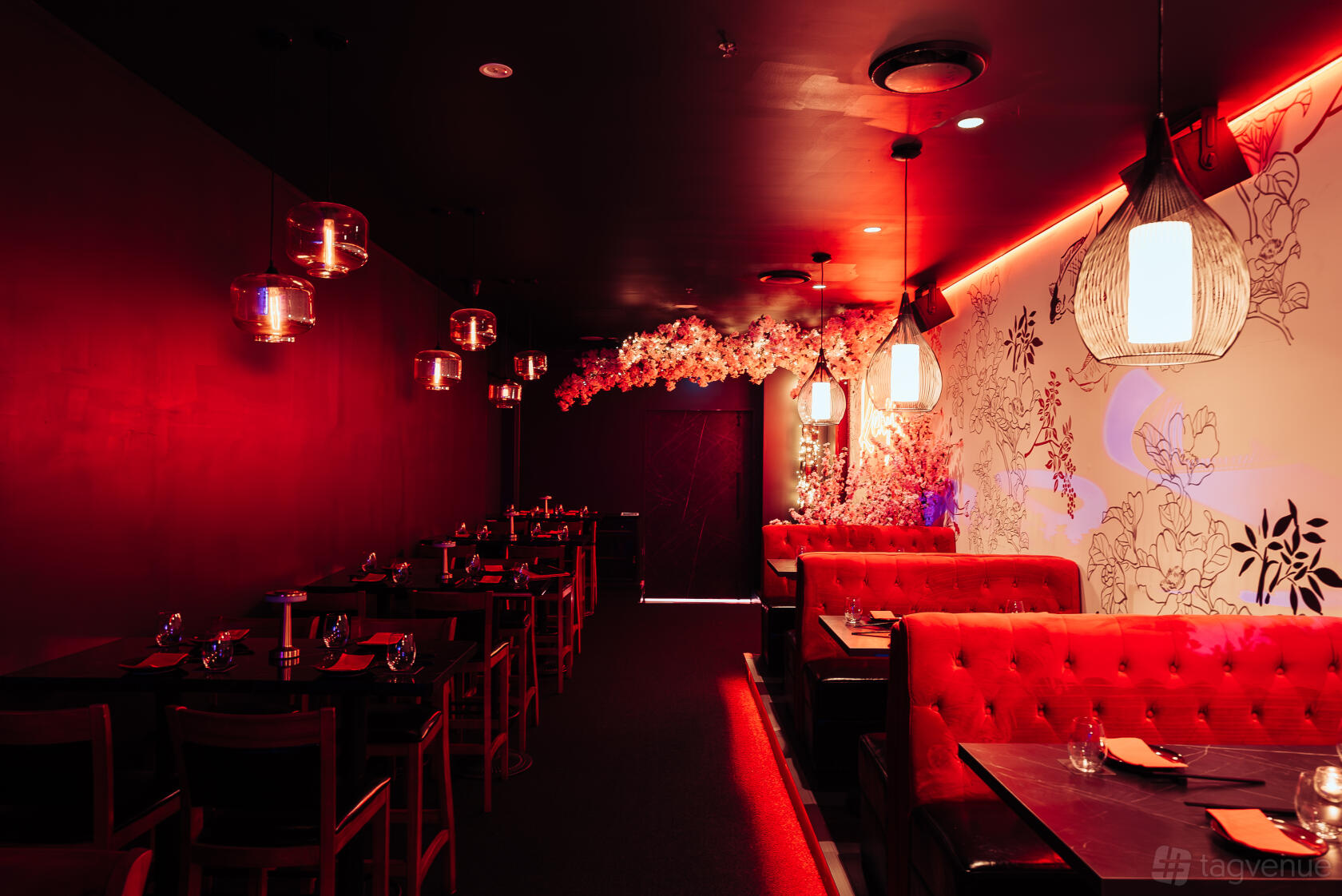 A restaurant with red upholstered banquettes, floral wall art, and pendant lighting at Kenjin.