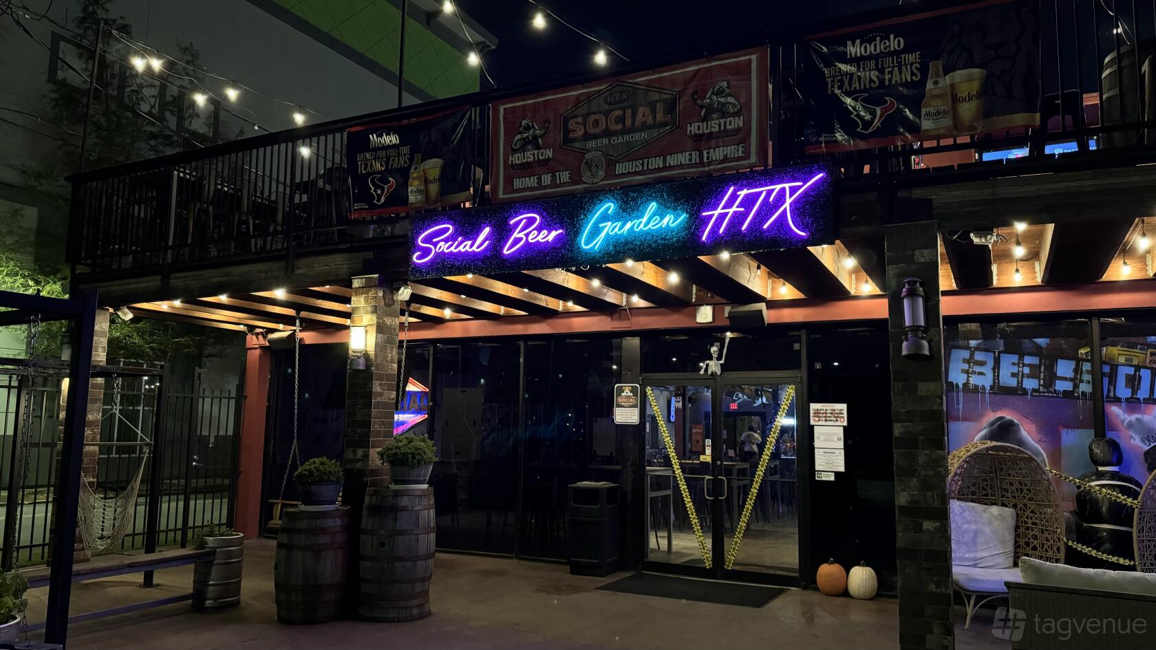 A pub exterior with neon signage, string lights, and large windows at Social Beer Garden HTX.