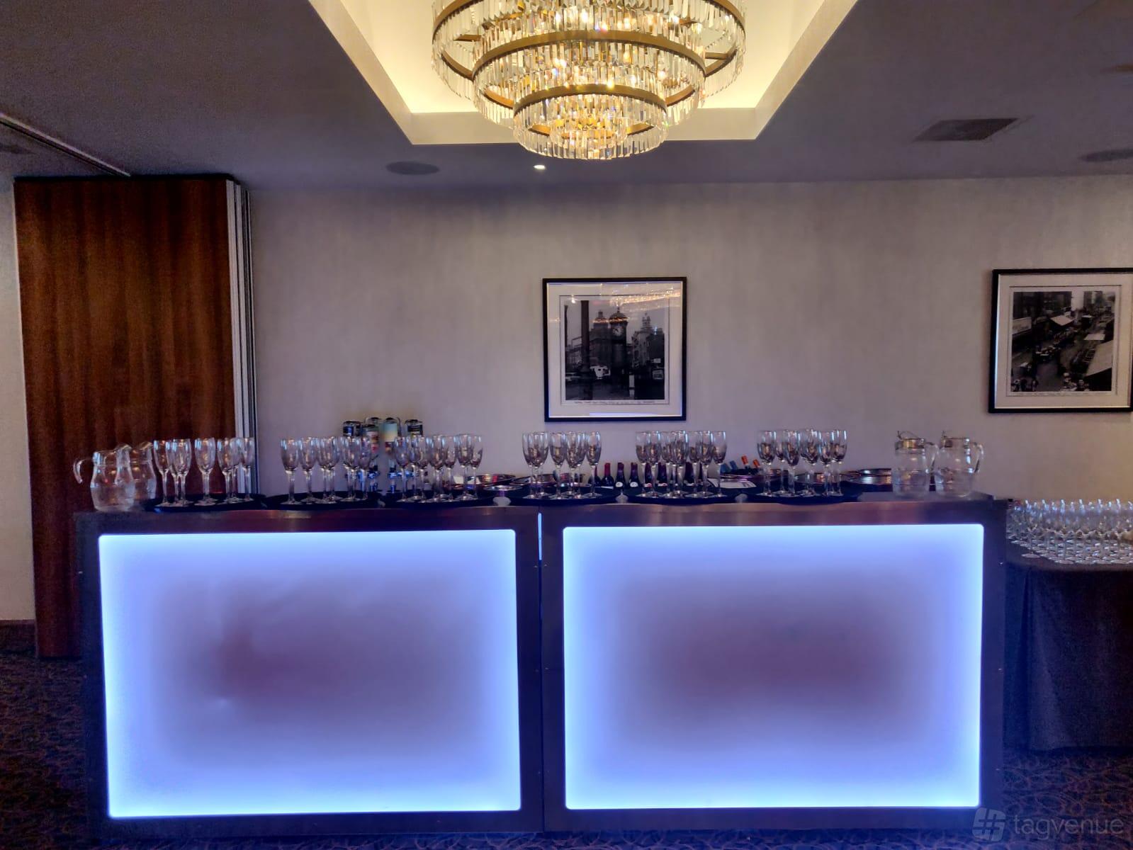 An event space with a glowing bar setup, glassware, and chandeliers at The Royal London Suites.