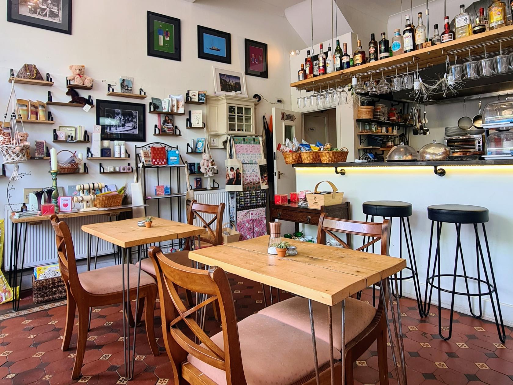 A cafe with wooden tables, wall shelves displaying gifts, and a bar counter with hanging glasses at Cool Carrot.