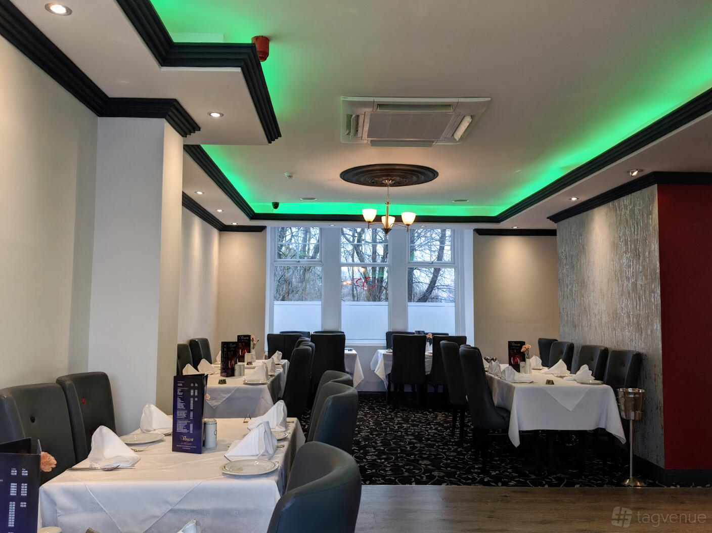 An event space in a restaurant with white tablecloths, upholstered chairs, and large windows at Voujon Restaurant.