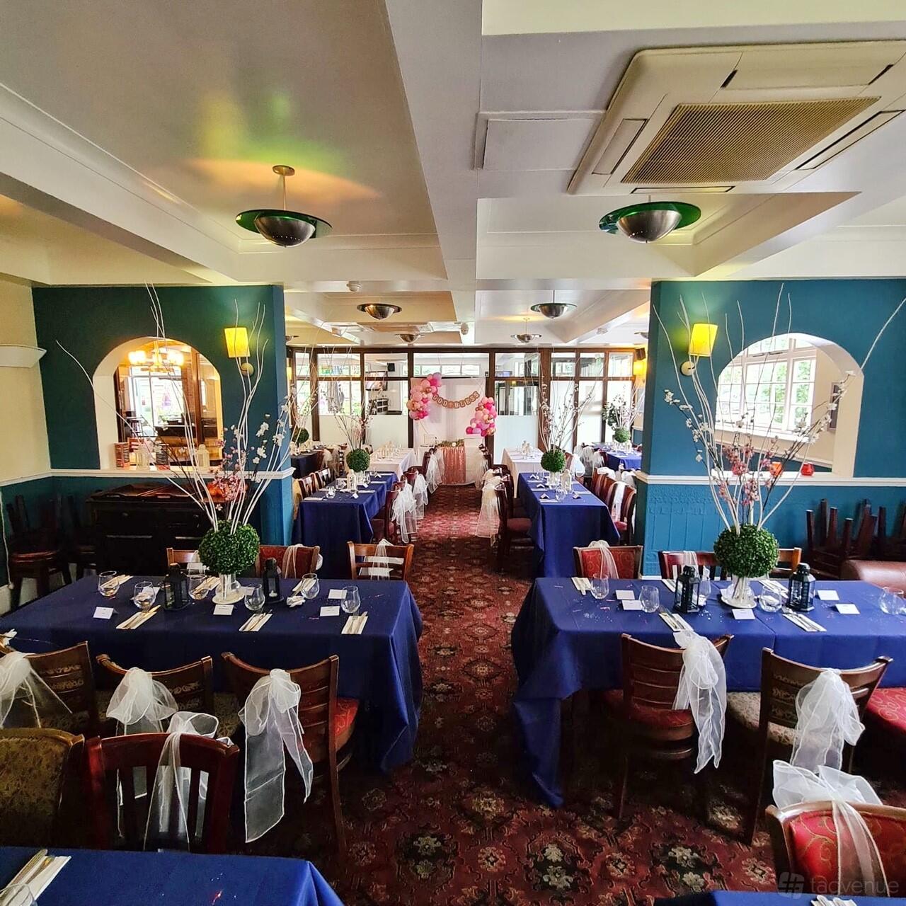 A pub dining room with long banquet tables covered in blue linens and decorative white chair sashes at Fox Connaught.