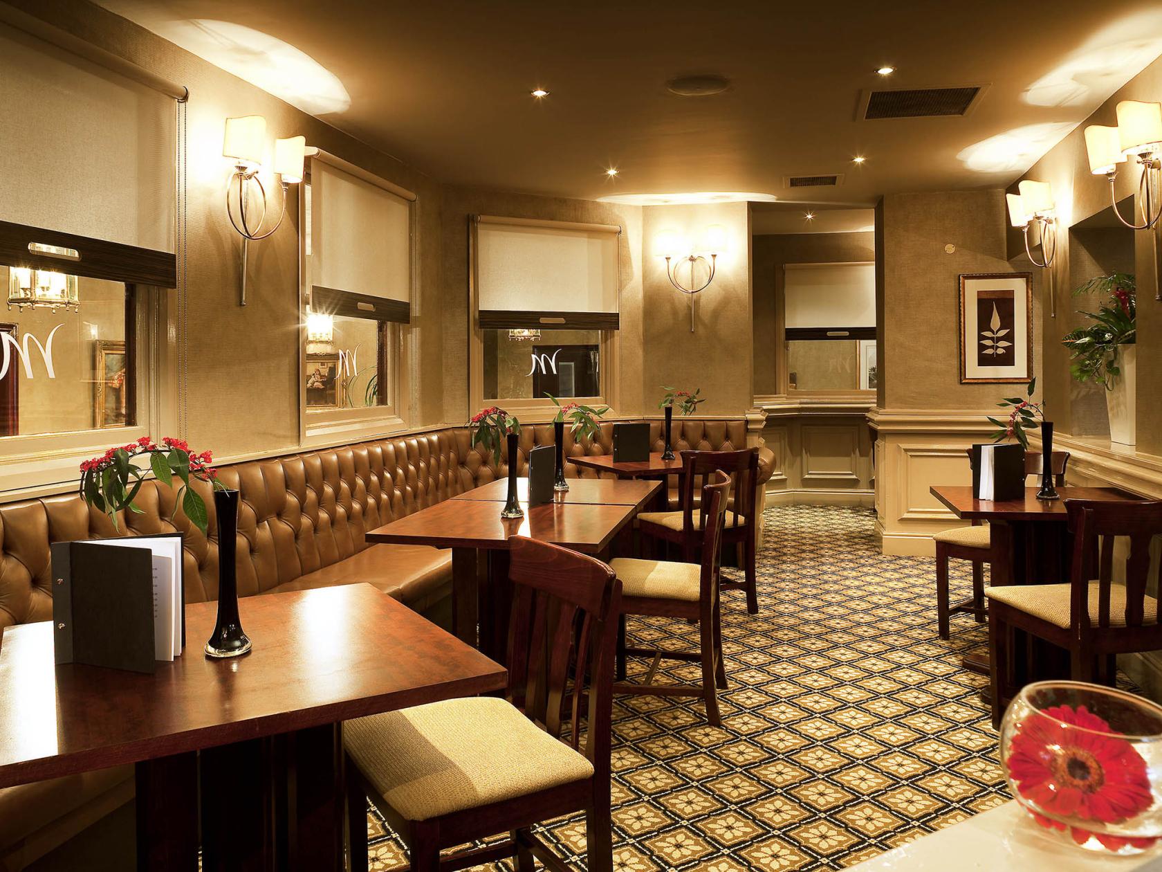 A hotel bar with tufted leather banquette seating, wooden tables, patterned carpet, and wall sconces at Mercure Norton Grange Hotel and Spa.