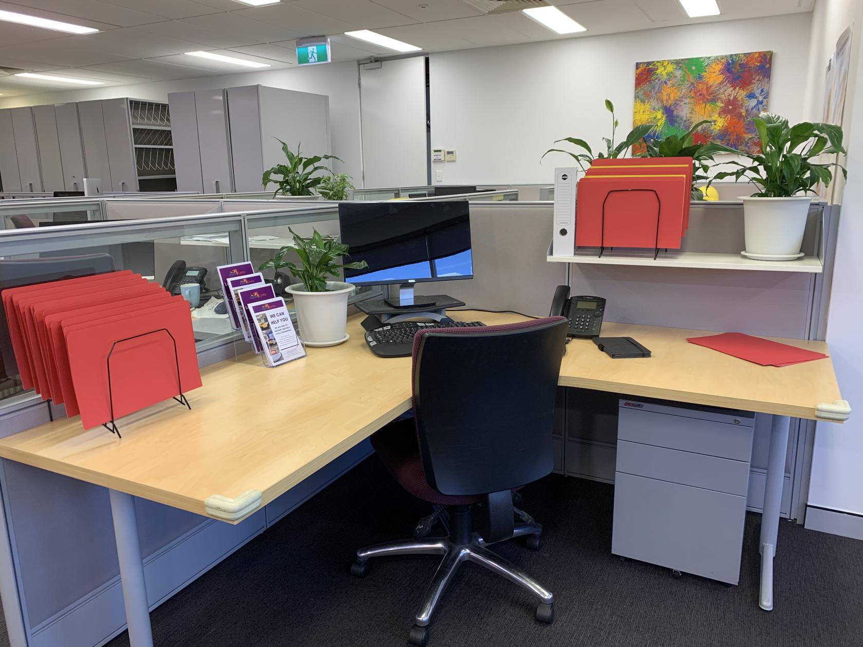 A coworking space with individual desk, office chair, desktop computer, file organizers, and desk plants at The Aspire Centre.