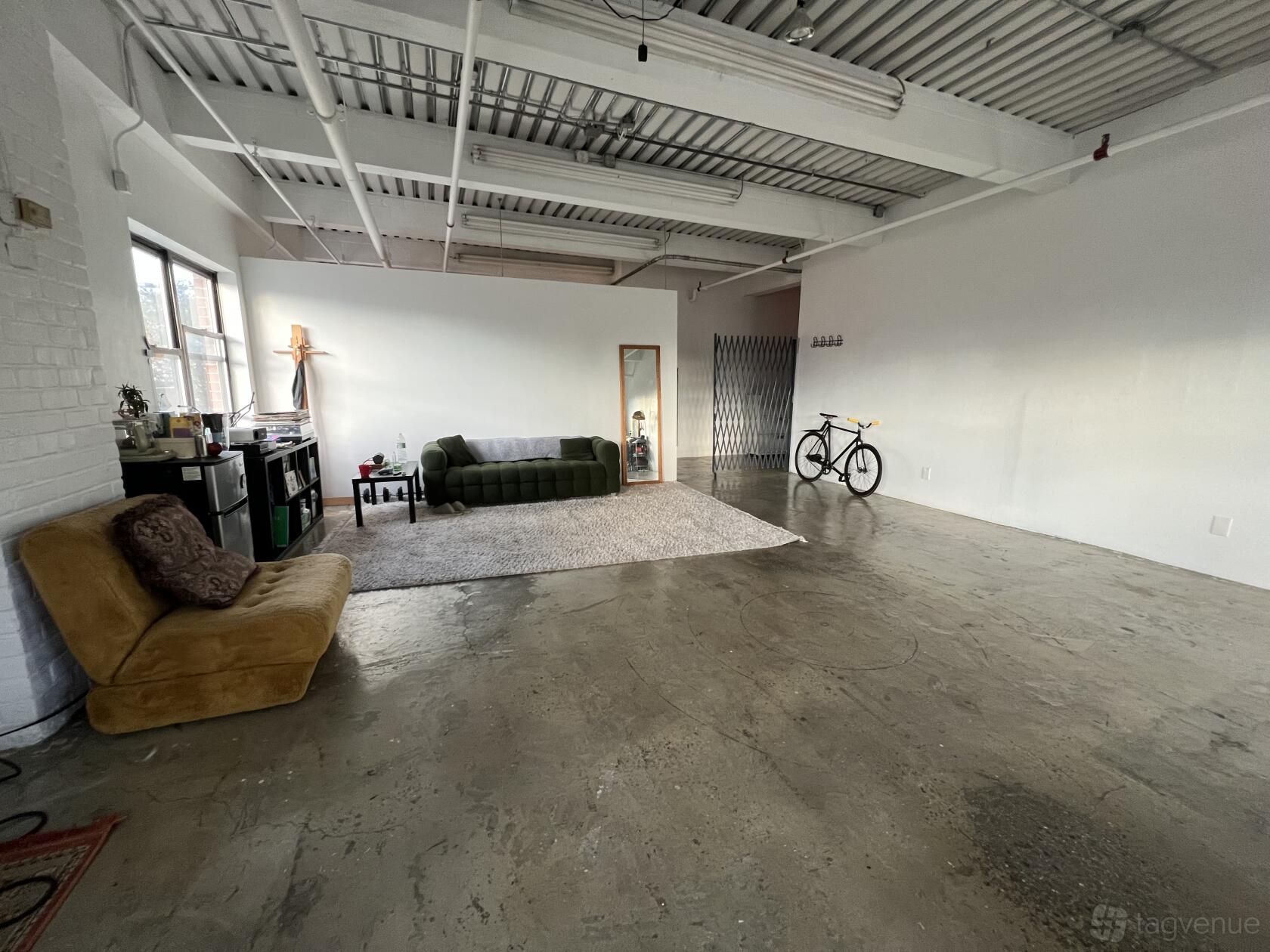 A coworking space with an open layout, polished concrete floors, sofas, and a large window at Primos Earthly Studios.