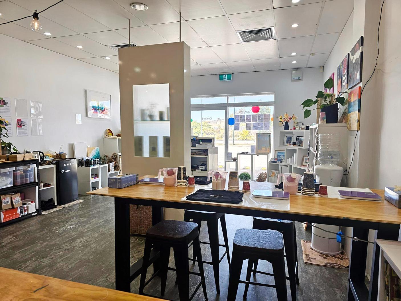 An event venue with wooden tables, art supplies, stools, and colorful artwork on white walls at iCreated Studio.